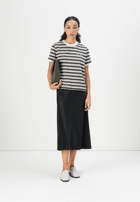 Stribet kortærmet skjorte i mørkegrøn og hvid, parret med en sort knælang nederdel. Modellen holder en mørkebrun clutch og har lyse sko på.