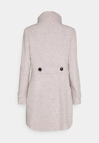 Ljusrosa ullkappa med en strukturerad yta, med hög krage, långa ärmar och två svarta knappar på baksidan.