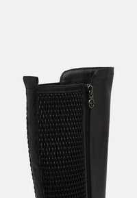Botín negro hasta el tobillo con un upper de cuero suave y detalle de malla texturizada, con un zipper lateral y acentos de hardware metálico.