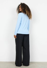 Bluza bleu deschis cu mâneci lungi, cu o textură netedă, asortată cu pantaloni negri largi. Bluza are un decolteu rotund și mâneci strânse pe brațe.