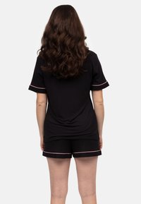 Zwarte T-shirt met korte mouwen en bijpassende shorts met roze details. Glad materiaal met een relaxte pasvorm, voorzien van omgekrulde mouwen en een open rugontwerp.