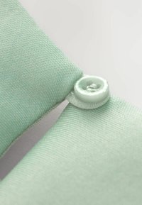 Mintgrön tyg med en subtil textur är vikt och säkrad med en matchande knapp. Knappen har en design med fyra hål.