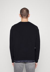Svart sweatshirt med rund halsringning och långa ärmar. Märkt logotyp i kontrasterande färger längst ner. Enkelt, slätt material.