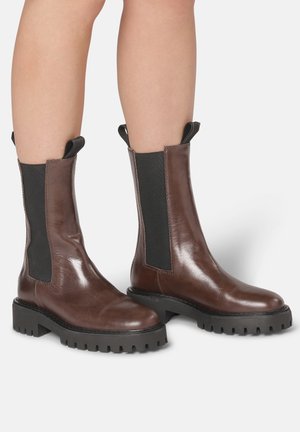 Bottines en cuir marron avec des panneaux élastiques sur les côtés, des tirettes et des semelles en caoutchouc texturé avec un motif de semelle épaisse.