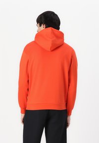 Orange hoodie with a drawstring hood, ribbed cuffs, and hem. Smooth fabric, relaxed fit, and a simple design. Black pants visible at the bottom.