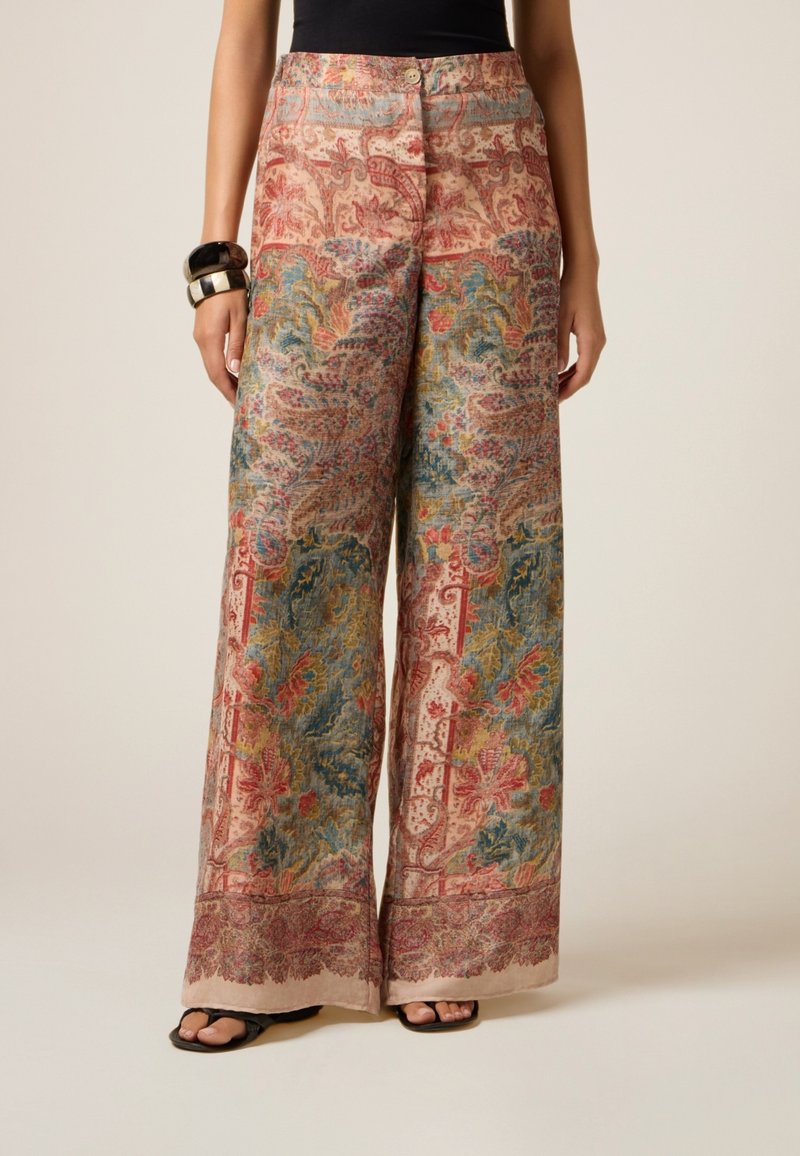 Pantaloni a gamba larga realizzati in tessuto stampato con intricate fantasie floreali in rosso, blu e verde su uno sfondo beige.