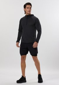 Maglietta sportiva nera a maniche lunghe con mezza zip, abbinata a pantaloni corti neri. Il tessuto sembra leggero e morbido. Scarpa sportive nere completano l'outfit.