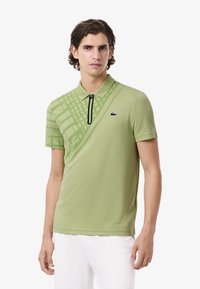 Camisa polo verde claro hecha de tela suave. Presenta un cuello con media cremallera, un sutil patrón de cuadrícula y un pequeño logotipo negro en el pecho.