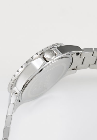 Montre en acier inoxydable argenté avec une lunette texturée et un boîtier rond. Comprend une couronne à poussoir marquée "BOSS" et un bracelet à maillons.