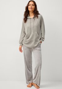 Hoodie en velours gris clair avec une poche avant et un cordon de serrage, associé à un pantalon large assorti. Texture douce, coupe décontractée.