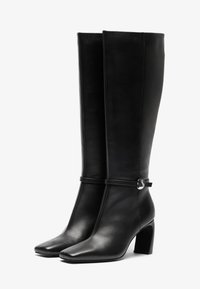 Black knee-high boots made of smooth leather with a square toe and chunky heel. Features a decorative strap with a silver-tone ring.