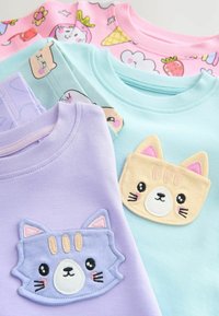 Quatre T-shirts pour enfants : lavande, vert menthe et rose, chacun ornés d'appliqués d'animaux mignons et de motifs colorés et ludiques.