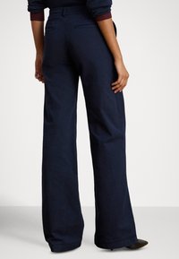 Mornarsko modre hlače širokih hlačnic iz bombažnega mešanega blaga, z oprijetim pasom, zadnjimi žepi in gladko teksturo z rahlim sijajem.