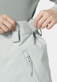 Světle šedé kalhoty mají pásek na suchý zip a boční kapsu na zip. Tkanina se zdá být hladká a vodoodolná, což je vhodné pro venkovní použití.