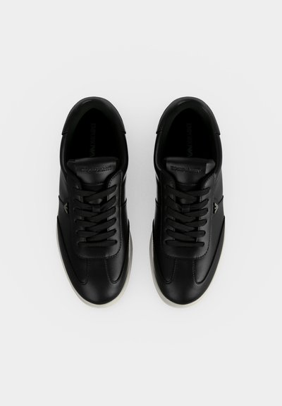 Ζευγάρι μαύρα δερμάτινα sneakers με κορδόνια και άσπρες σόλες, από ψηλά σε λευκό φόντο.
