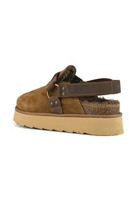Scarpa slip-on in suede marrone con una suola piatta in sughero testurizzato, cinturino in pelle con accenti metallici e un morbido rivestimento in pelliccia interna.