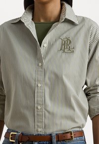 Csíkos gombos ing zöld és fehér színben, hímzett logóval a mellrészen, klasszikus gallérral és feltűrhető ujjakkal.