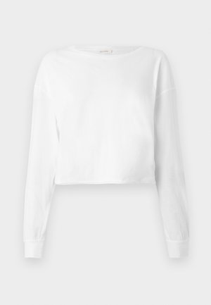 Chemise cropped blanche à manches longues avec un col rond et des poignets ajustés, présentée sur un fond blanc.