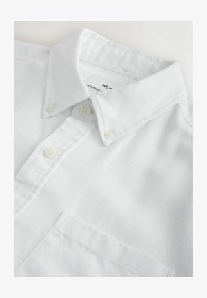 Fehér, gombos ing strukturált gallérral, sima szövet textúrával, mellkasi zsebbel és apró gombokkal az elején.