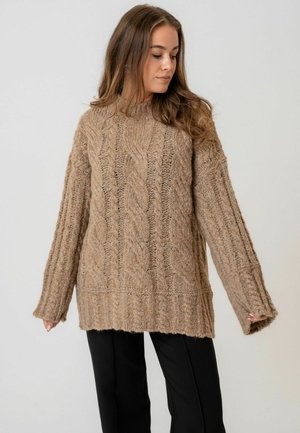 Üks suur, tekstuuriga kudum, helepruun, millel on kaablipatternid. Sellel on pikad varrukad ja lai soonikäär. Kombineeritud mustade pükstega.