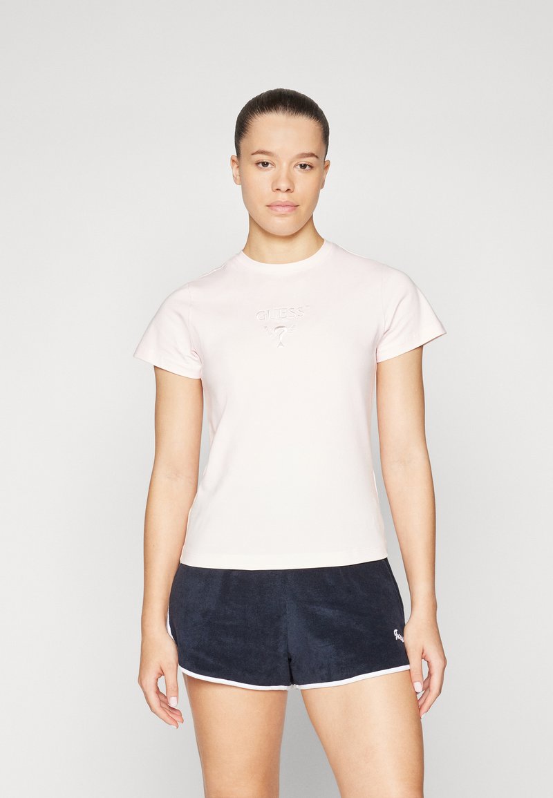 Lyserød kortærmet t-shirt med rund hals, med et præget "GUESS" logo. Kombineret med mørkeblå frottéshorts med hvid kant.