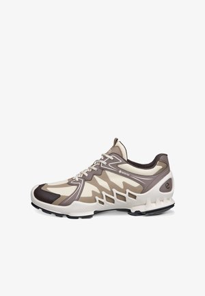 Chaussure de sport beige clair et marron avec tissu Gore-Tex, design à lacets, semelle texturée et détails géométriques découpés sur le côté.