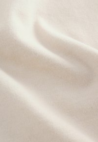 Flødefarvet stof med en fin ribbet struktur, der viser bløde folder og en glat overflade, hvilket indikerer et let og elastisk materiale.