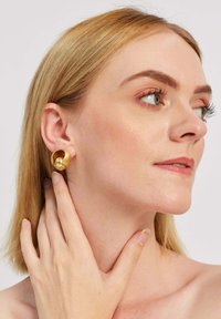 Zelta metāla auskari ar unikālu, abstraktu dizainu. Gluda, pulēta virsma ar apaļu formu, valkāti kreisajā ausī.