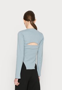 Blusa de manga longa, azul-claro, com textura canelada, detalhe de costas com recorte e decote arredondado, combinada com calças pretas.