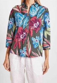 Camisa de botones con estampado floral y mangas tres cuartos. Presenta flores vibrantes en tonos rosa, azul y verde sobre un fondo verde oscuro. Material de algodón.