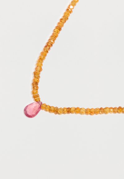 Collier de perles orange facettées avec un pendentif unique facetté en forme de goutte rose sur fond blanc.