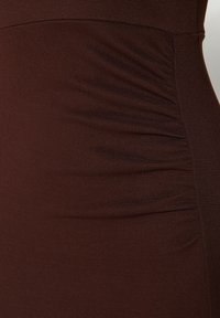 Hnědý proužkovaný šat s nabíranými detaily na jedné straně, který zvýrazňuje strukturu a těsně přiléhající design.