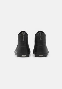 Zapatillas altas negras de cuero. Presentan tiradores etiquetados como "WASTED" y "TALENT". Suela de goma con la marca "GLOBE".