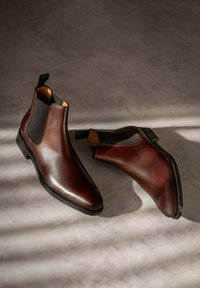 Bottines Chelsea en cuir marron avec des panneaux latéraux élastiques, des bouts arrondis épurés et une languette pour un enfilage facile. Fini texturé avec un éclat subtil.