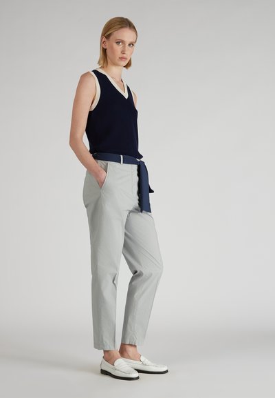 Haut sans manches bleu marine avec un col en V crème, pantalon léger gris sur mesure et mocassins blancs. Les pantalons comportent des poches latérales et un accent ceinture bleu marine.