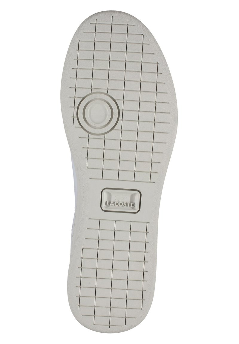 Biała gumowa podeszwa butów z teksturowanym wzorem siatki i okrągłym bieżnikiem. Zawiera widoczne logo Lacoste umieszczone centralnie w pobliżu pięty.