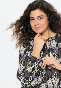 Blusa nera con motivo, arricchita da disegni verdi, viola e bianchi; presenta un colletto con lacci e maniche lunghe con polsini elasticizzati.