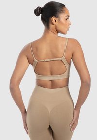 Lys brun sports-bh med justerbare stropper og en åben rygdesign. Stof er glat og ribbet, kombineret med højtaljede leggings.