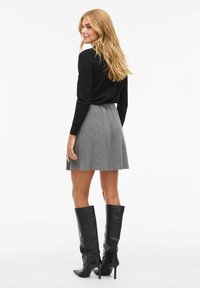 Černý dlouhý rukáv v kombinaci se šedou plisovanou sukní a černými koženými kozačkami na podpatku až ke kolenu. Pohled zezadu zdůrazňuje vrstvení oblečení.