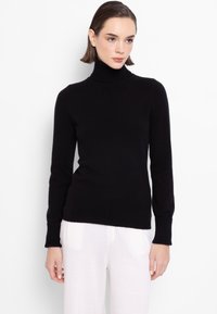 Črna pulover z visokim ovratnikom, ki ima oprijet kroj, rebrast ovratnik in manšete, narejen iz gladkega, mehkega materiala. V kombinaciji s svetlimi hlačami.