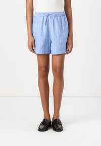 Shorts en lin mélangé bleu clair avec des rayures blanches verticales, taille élastique et coupe ample. Associés à des mocassins noirs.