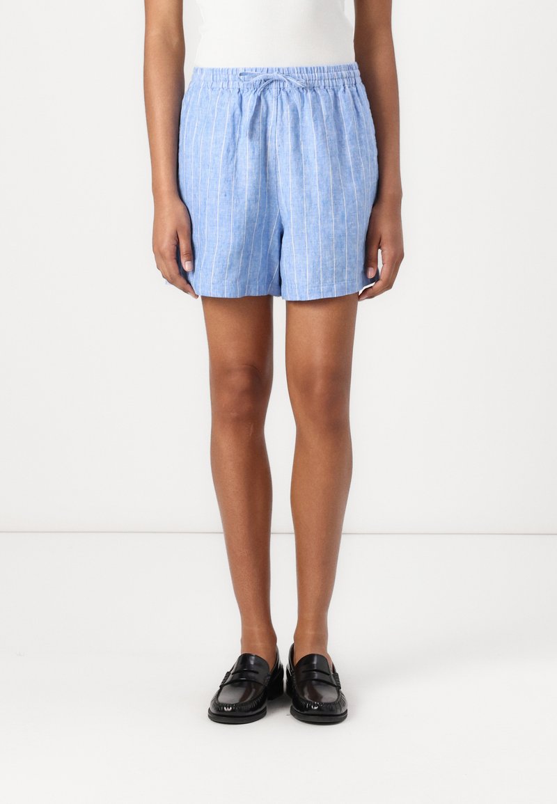Shorts en lin mélangé bleu clair avec des rayures blanches verticales, taille élastique et coupe ample. Associés à des mocassins noirs.