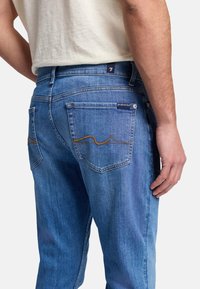 Jean en denim bleu clair au design classique, avec deux poches arrière et des coutures contrastées en motif ondulé. Fabriqué en denim doux et texturé.