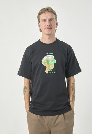 Black cotton t-shirt featuring a graphic print of a green-faced character with sunglasses. Text "LIVE SLOW" and "DIE OLD" in green above and below.
