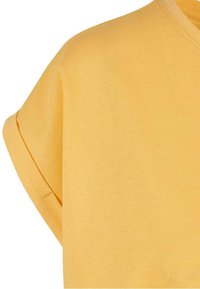 Chemise jaune à manches courtes avec détail de manche retroussée et couture visible sur un fond uni.