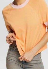 Peachfarvet strikket sweater med korte ærmer, der har en ribbet lyserød krave og manchetter, med en afslappet pasform og glat tekstur.