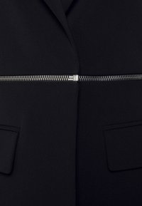 Czarna kurtka z srebrnym poziomym zamkiem błyskawicznym w środkowej części oraz dwiema kieszeniami z klapami po obu stronach.