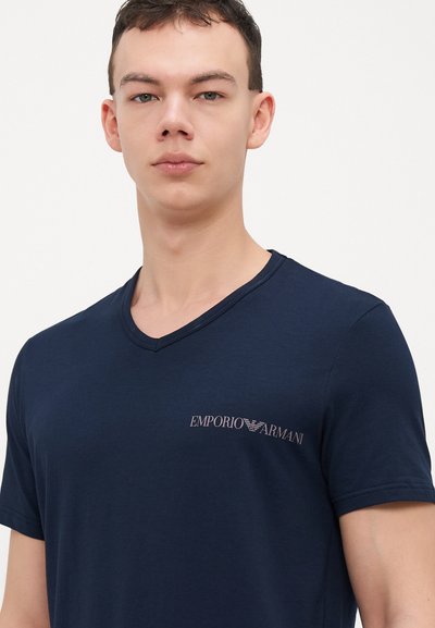 Námornícka modrá v-neck tričko vyrobené z mäkkého materiálu s podpisovým logom Emporio Armani v svetlej farbe na ľavej strane hrudníka.