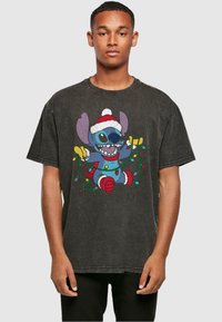 Camiseta negra de gran tamaño, con un personaje de dibujos animados colorido que lleva un gorro de Santa, rodeado de luces navideñas. Textura de tela suave y desgastada.