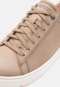 Μπεζ δερμάτινο αθλητικό παπούτσι με μπεζ κορδόνια, λεπτομερείς ραφές και λευκή λαστιχένια σόλα. Το «BIRKENSTOCK» είναι ανάγλυφο στη γλώσσα.